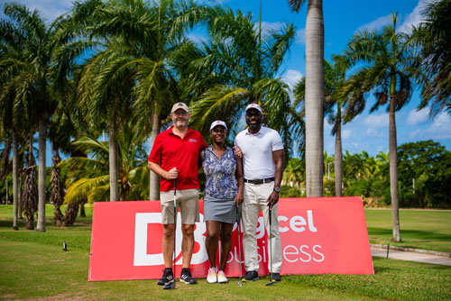 Three golfers smiling together in front of a Digicel Business Sign