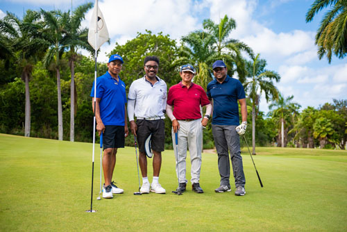 Four golfers smiling together with palm trees in the background