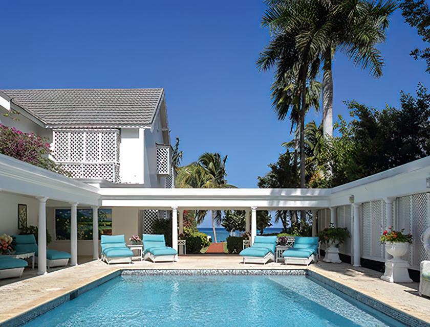 A pool with lounge chairs and a house with a beach and trees