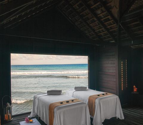 Two beds with white sheets on each side with a view of the ocean